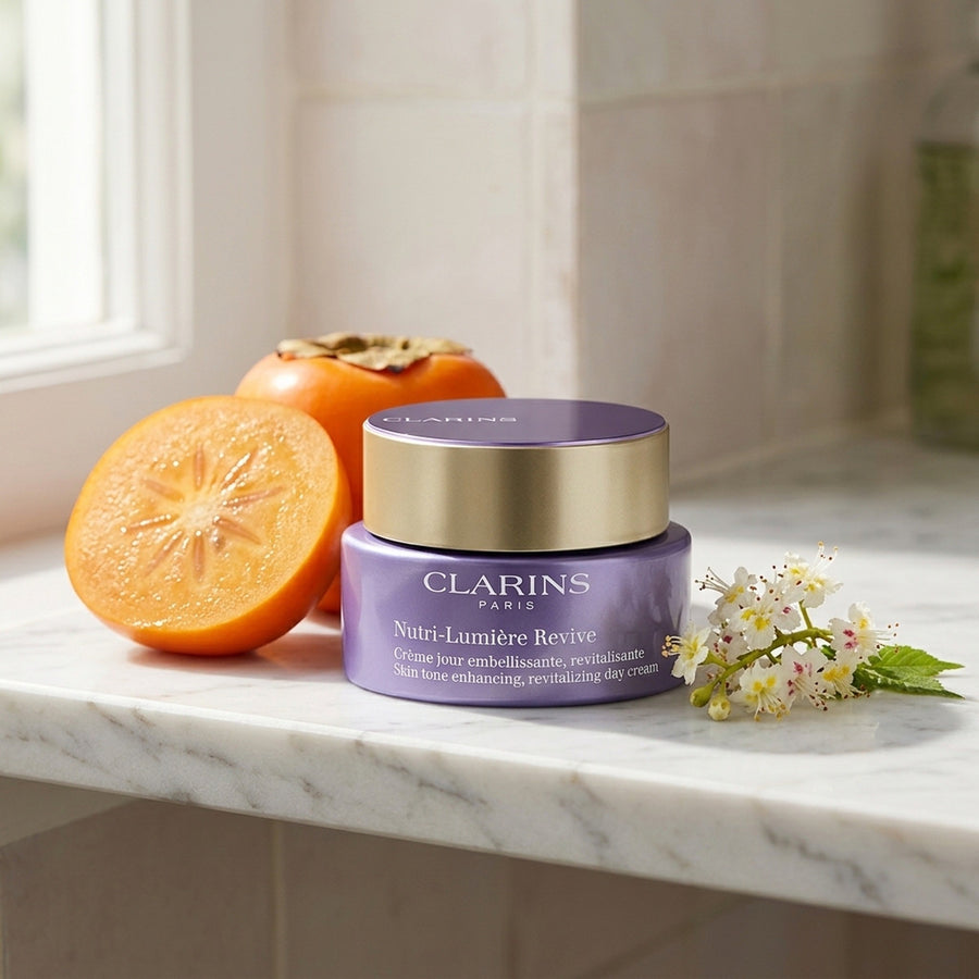 Clarins Nutri-Lumière Revive en un estante de mármol con caqui y flor de castaño