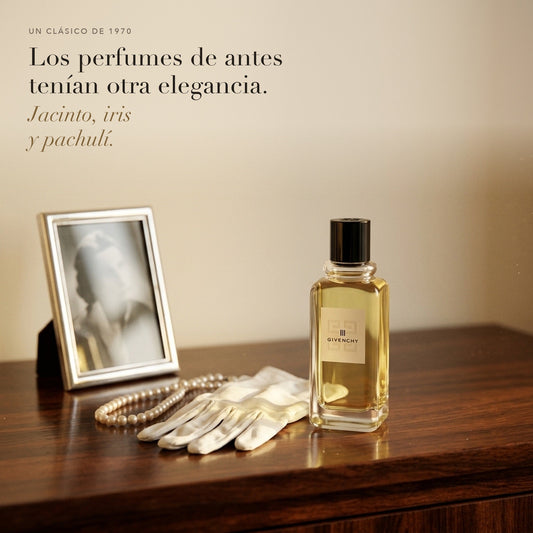 Givenchy III en un tocador de madera con guantes blancos, perlas y una foto antigua