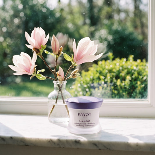 Crema de día Payot Suprême en el alféizar de una ventana junto a una rama de magnolia